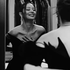 a woman in a black dress is looking at herself in the mirror and she has her hands on her chest