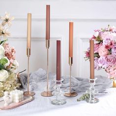 a table topped with vases filled with pink flowers and gold candlestick holders next to each other