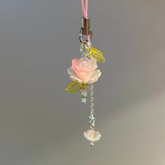 a pink and white rose hanging from a chain with beads on it's end