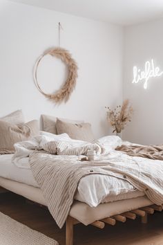 a bed with white linens and pillows in a room that has a wreath on the wall