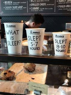 coffee cups with words on them are sitting in front of a display case at a bakery