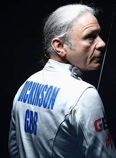 an older man with grey hair is holding a bow and looking at the camera while standing in front of a black background