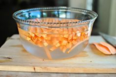 a bowl filled with sliced carrots on top of a wooden cutting board