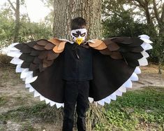 a young boy wearing an eagle costume standing in front of a tree