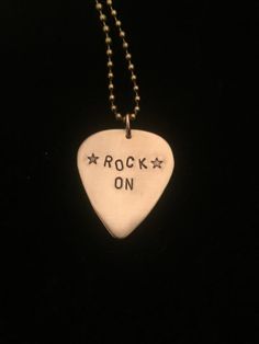 a white guitar pick with the words rock on written on it, hanging from a ball chain