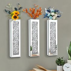 three decorative mirrors mounted to the side of a wall with flowers and plants in them