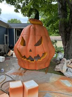 a large pumpkin sitting in the middle of a yard next to a tree and some boxes