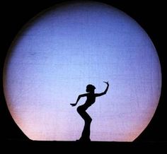 the silhouette of a woman dancing in front of a large sun with her arms outstretched