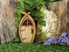 a wooden fairy door in the grass next to purple flowers