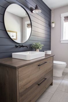 a white toilet sitting next to a wooden dresser in a bathroom under a round mirror