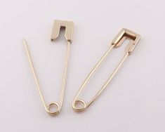 two pairs of gold colored metal clips on a white surface, one has a hook and the other has a pair of scissors