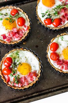 four pies with eggs, tomatoes and meat on them sitting on a baking sheet