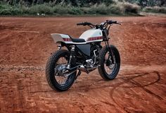 a white and black motorcycle parked on top of a dirt covered field with trees in the background