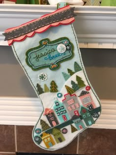 a christmas stocking hanging on the wall in front of a fireplace with a house and trees