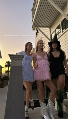 three women in short dresses and boots posing for the camera on a porch at sunset