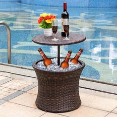 an outdoor table with bottles of wine and ice in it next to a swimming pool