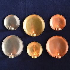 four copper plates with candles in them on a blue surface