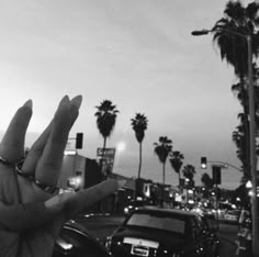 a hand holding something up in the air with palm trees and cars parked on the side of the road