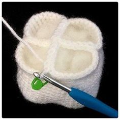 a pair of white knitted baby booties with a blue handled crochet hook