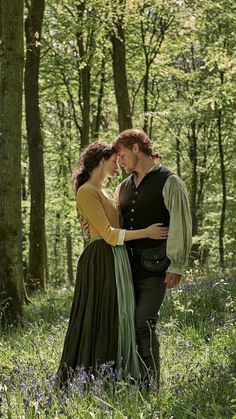 a man and woman are standing together in the woods with bluebells around them