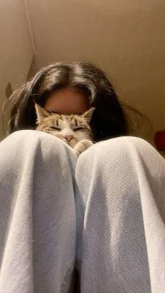 a woman laying on her stomach with a cat in her lap behind her back, looking at the camera