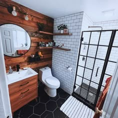 a white toilet sitting next to a walk in shower under a bathroom mirror and sink