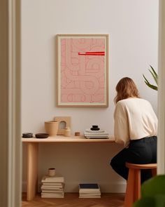 a woman sitting at a desk in front of a framed art piece on the wall