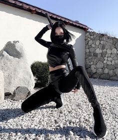 a woman in black outfit and boots posing on rocks with her leg up to the side