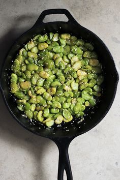 a skillet filled with green beans on top of a white counter next to a black spatula