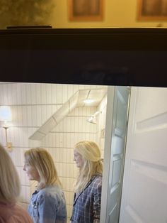 two women standing in front of a mirror looking at their own reflection on the wall