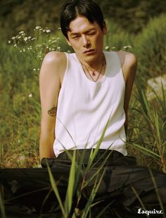 a young man sitting in the grass with his eyes closed, wearing a white tank top and black pants