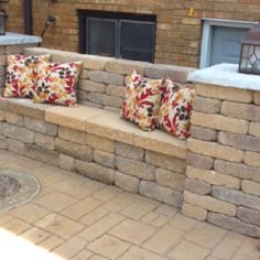 some pillows are sitting on a stone bench near a brick wall and fire place in the back yard