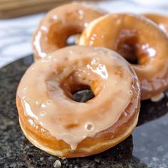 three glazed donuts sitting on top of a black plate