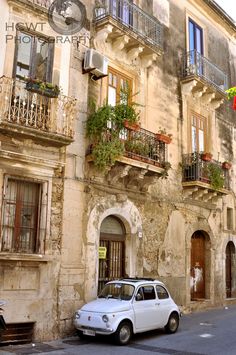 an old white car parked in front of a building with balconies on the windows