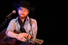 a man wearing a cowboy hat and playing an acoustic guitar