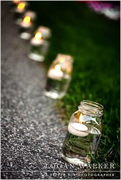 several mason jars filled with candles sitting on the side of a road next to grass