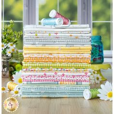 a stack of colorful fabrics sitting on top of a wooden table next to a window