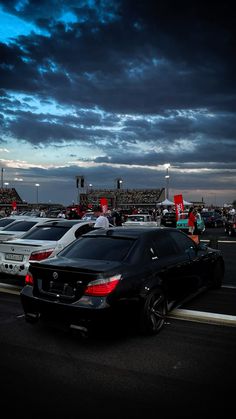 several cars are parked on the side of the road under a dark sky with clouds