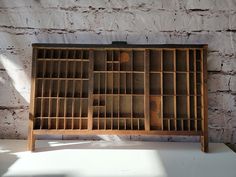 an old wooden book case sitting on top of a white table next to a brick wall