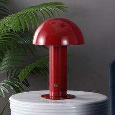 a red lamp sitting on top of a white table next to a green leafy plant