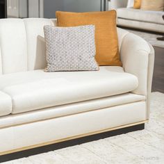 a white couch with two orange pillows on it's back and a coffee table in the background