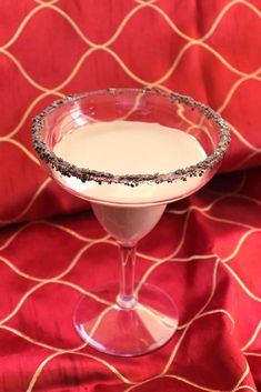 a drink in a wine glass on a red cloth with silver flecks around the rim