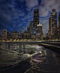 the city skyline is lit up at night with lights reflecting in the water and clouds