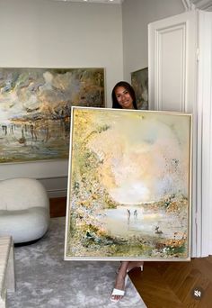 a woman holding up a large painting in her living room