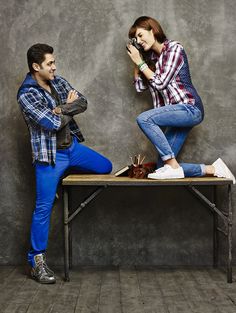 a man and woman sitting on top of a table next to each other while taking pictures