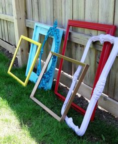 four different colored frames sitting in the grass next to a wooden fence with string on it