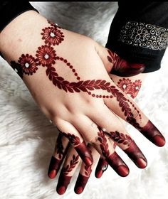 a woman's hand with henna tattoos on her left arm and hands, both decorated with red flowers