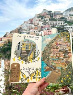 a person holding up an open book in front of a view of a town and the ocean