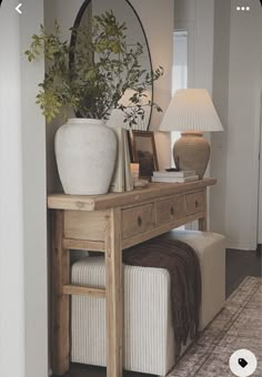 a wooden table topped with a white vase next to a lamp and a mirror on top of it