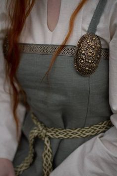 a woman with red hair wearing a gray dress and gold brooch on her belt